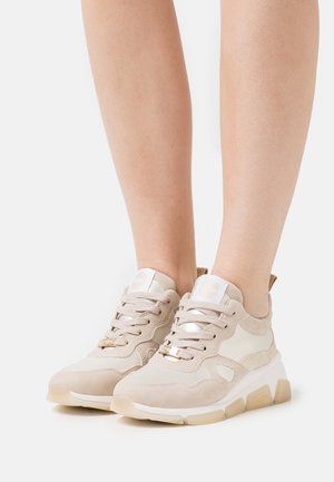 Beige sneakers featuring a mix of suede and leather, round toe design, padded collar, and a textured rubber sole with gold accents.