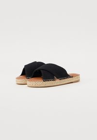 Sorte vevde stoffsandaler med kryssremmer, naturlig jute såle, flat design og kontrasterende brun fotbunn.