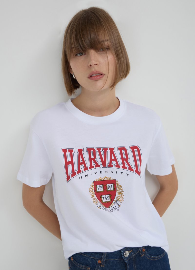 T-shirt bianco in cotone con testo rosso "HARVARD UNIVERSITY" e design dello stemma, scollo rotondo e maniche corte.