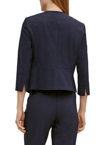 Marineblaue maßgeschneiderte Jacke mit Dreiviertelärmeln, Rückennahtdetails und seitlichen Schlitzen am Saum. Glatte Stoffstruktur.