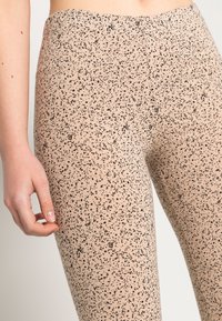 Leggings bege com um padrão preto salpicado, cintura elástica, textura suave, cintura alta e design ajustado.