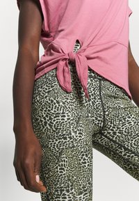 Rosa knyttröja med korta ärmar, ihop med figurnära leggings med svart och grön djurmönsterdesign och kontrasterande sömmar.