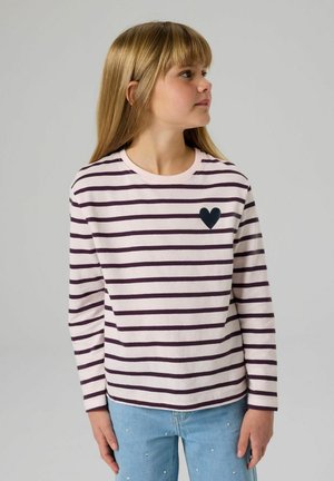 Gestreiftes Langarmshirt in blassem Rosa und Dunkellila, mit einem schwarzen Herzaufnäher auf der linken Brust. Kombiniert mit hellblauen, verzierten Jeans.