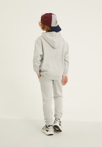 Gai pelēks džemperis ar kapuci un atbilstošas bikses, kas izgatavotas no mīksta materiāla, ar kenguru kabatu un ribota mala, kombinētas ar daudzkrāsu cepuri.