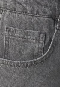Tela de mezclilla gris oscuro que presenta un bolsillo trasero con costuras visibles. El bolsillo tiene una forma rectangular y un patrón texturizado sutil.