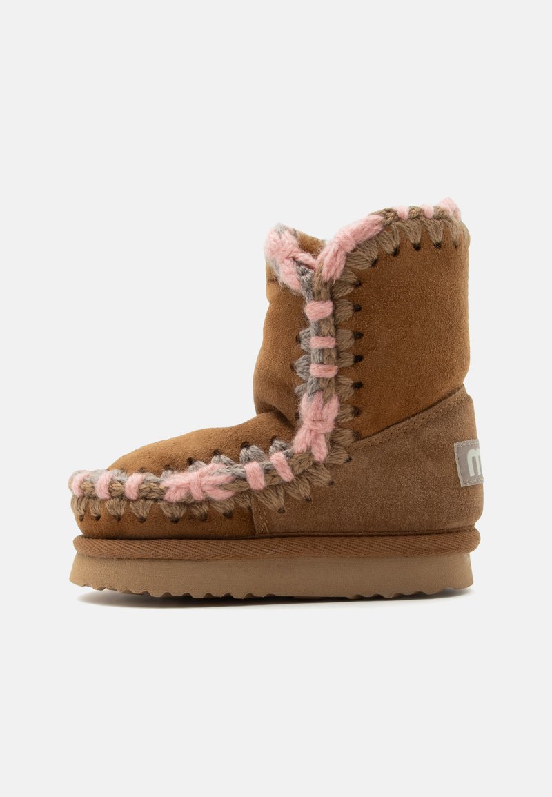 Botte d'hiver en daim marron avec une épaisse surpiqûre rose et grise le long des coutures, semelle plate et écusson logo sur le talon.