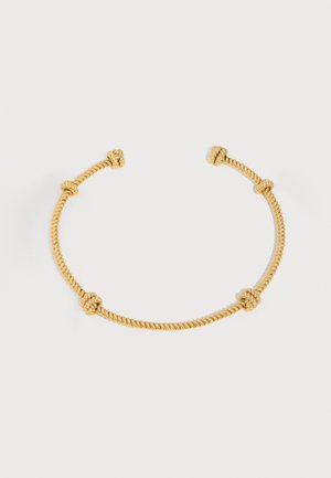 Brățară aurie tip sfoară răsucită, deschisă, cu noduri decorative amplasate uniform pe un fundal simplu, deschis la culoare.