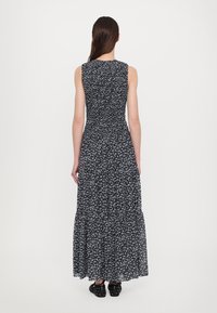 Maxime dress in black with small white floral pattern. Features a fitted bodice, sleeveless design, and a tiered ruffle hem. Smooth fabric texture.
