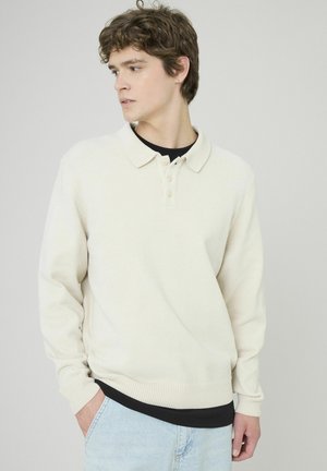 Pull en maille crème avec un tissu texturé, un col et une patte de boutonnage à trois boutons. Présente des manches longues ainsi que des poignets et un ourlet côtelés.