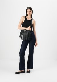 Black leather shoulder bag with fringes, buckle detail, and adjustable strap. Paired with dark blue flared jeans and black ballet flats.