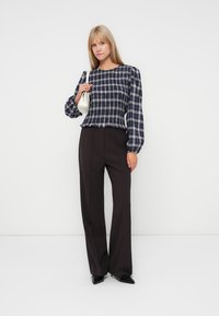 Blusa a scacchi navy e bianca con maniche a sbuffo, abbinata a pantaloni neri a vita alta e una piccola borsa bianca. Texture lisce.