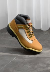 Brown suede hiking boot with gray accents, padded collar, yellow laces, and a rubber sole. Features logo detail and contrasting stitching.