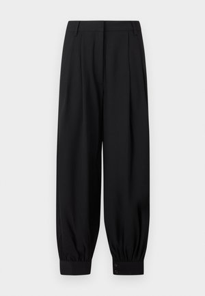 Melnas bikses ar augstu jostasvietu, krokām, pogājamiem potīšu manžetēm, jostas cilpām un vaļēju, sašaurinātu piegriezumu uz baltas fona.