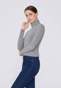 Maglione a collo alto grigio in tessuto morbido, design aderente con maniche lunghe, abbinato a jeans blu scuro con tasche e silhouette slim.