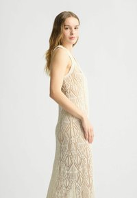 Lungo abito in pizzo crema con motivi geometrici, caratterizzato da un design senza maniche e una silhouette aderente. Texture morbida e materiale leggero.
