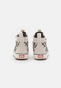 Höga sneakers i ljusgrå mocka med svart rutmönster, vit sula och röd logotyp på hälen. Har dubbla dragflikar.