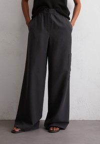 Wijduitlopende broek van donkergrijs stof, met een enkele zijzak en een elastische tailleband met knoopsluiting. Soepele textuur.