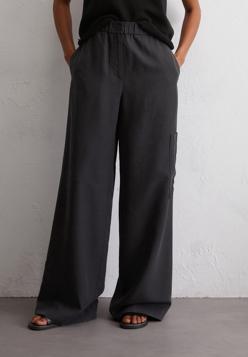 Wijduitlopende broek van donkergrijs stof, met een enkele zijzak en een elastische tailleband met knoopsluiting. Soepele textuur.