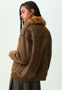 Giacca in ecopelle marrone con collare morbido, polsini elasticizzati e vestibilità rilassata. Caratterizzata da una texture liscia e dettagli di cucitura minimi.