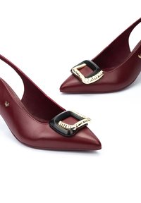 Tacones slingback de punta en color marrón con hebillas decorativas cuadradas en negro y dorado sobre un fondo blanco.