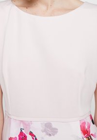 Donna che indossa un vestito rosa chiaro con un corpetto aderente e una gonna a fantasia floreale nei toni del rosa, viola e bianco.