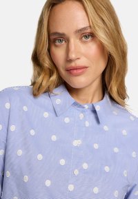 Chemise bleu clair à rayures avec pois blancs, col classique et fermeture à boutons. Présente une texture lisse et une coupe décontractée.