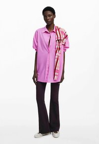 Vaaleanpunainen ylimittainen lyhythihainen pusero, yhdistetty tummiin liehuviin housuihin. Raidallinen huivi roikkuu yhdellä olkapäällä.