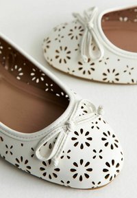 Ballerine in pelle bianca con design floreali intagliati al laser, punta rotonda e dettaglio a fiocco sul davanti. Fodera interna liscia.