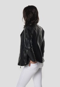 Čierna kožená motocyklová bunda s rebrovanými akcentmi na pleciach, vreckami so zipsom a elegantným dizajnom, kombinovaná s bielymi nohavicami.