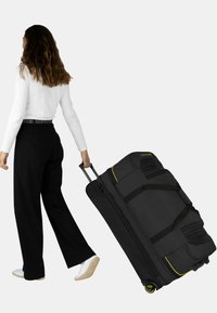 Schwarze Rollreisetasche mit gelben Akzenten, strapazierfähigem Gewebe, mehreren Taschen, großen Rädern und ausziehbarem Griff für einen einfachen Transport.