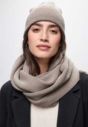 Beige ribbad stickad mössa och oändlighetsscarf, strukturerad med subtila glitters, kombinerad med en mörk kappa och en ljus tröja.