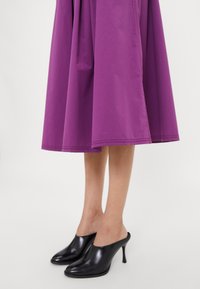Vestido midi morado con un dobladillo acampanado, combinado con elegantes mules negros de punta abierta que presentan una punta afilada y un alto tacón de aguja.