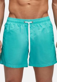 Shorts de bain turquoise avec une taille élastique, fermeture à cordon et poches latérales. Matière lisse et légère, longueur au-dessus du genou.