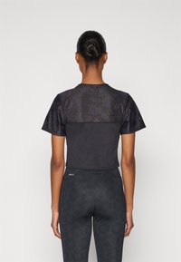 Top atlético negro recortado con tejido texturizado en los hombros y sección inferior suave. Combinado con legging oscuros con estampado.