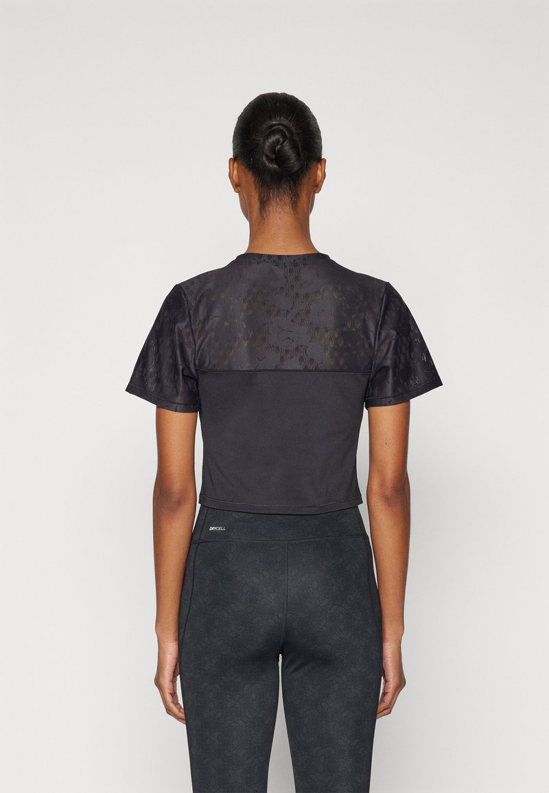 Zwarte sportieve crop top met textuurstof op de schouders en een gladde onderkant. Gecombineerd met donkere, gemusterde leggings.