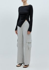 Zwart lange mouwen top met een aansluitende pasvorm, geplooide zijdetails en knoopaccenten. Gepaard met lichtgrijze wijde cargo-broek.