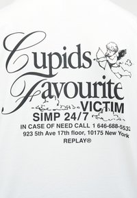 Κείμενο σε λευκό ύφασμα που αναγράφει «Το Αγαπημένο Θύμα του Έρωτα Simp 24/7» με ένα μικρό σχέδιο έρωτα που στοχεύει με βέλος, και στοιχεία επικοινωνίας από κάτω.