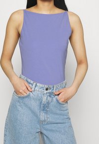 Lila ärmlös bodysuit i mjukt tyg, kombinerad med högmidjade ljusblå jeans med en sliten look och framfickor.