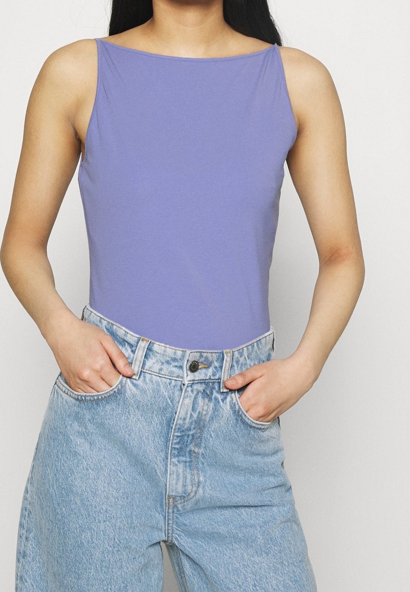 Lila ärmlös bodysuit i mjukt tyg, kombinerad med högmidjade ljusblå jeans med en sliten look och framfickor.