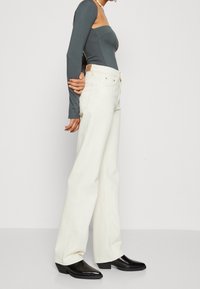 Camiseta ajustada de manga larga en gris oscuro, combinada con jeans blancos de pierna ancha y cintura alta. Botines negros de tacón completan el conjunto.