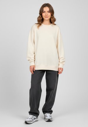 Sweatshirt beige clair avec une coupe décontractée et un col rond. Associé à un jean baggy gris foncé et des baskets grises. Texturé lisse.