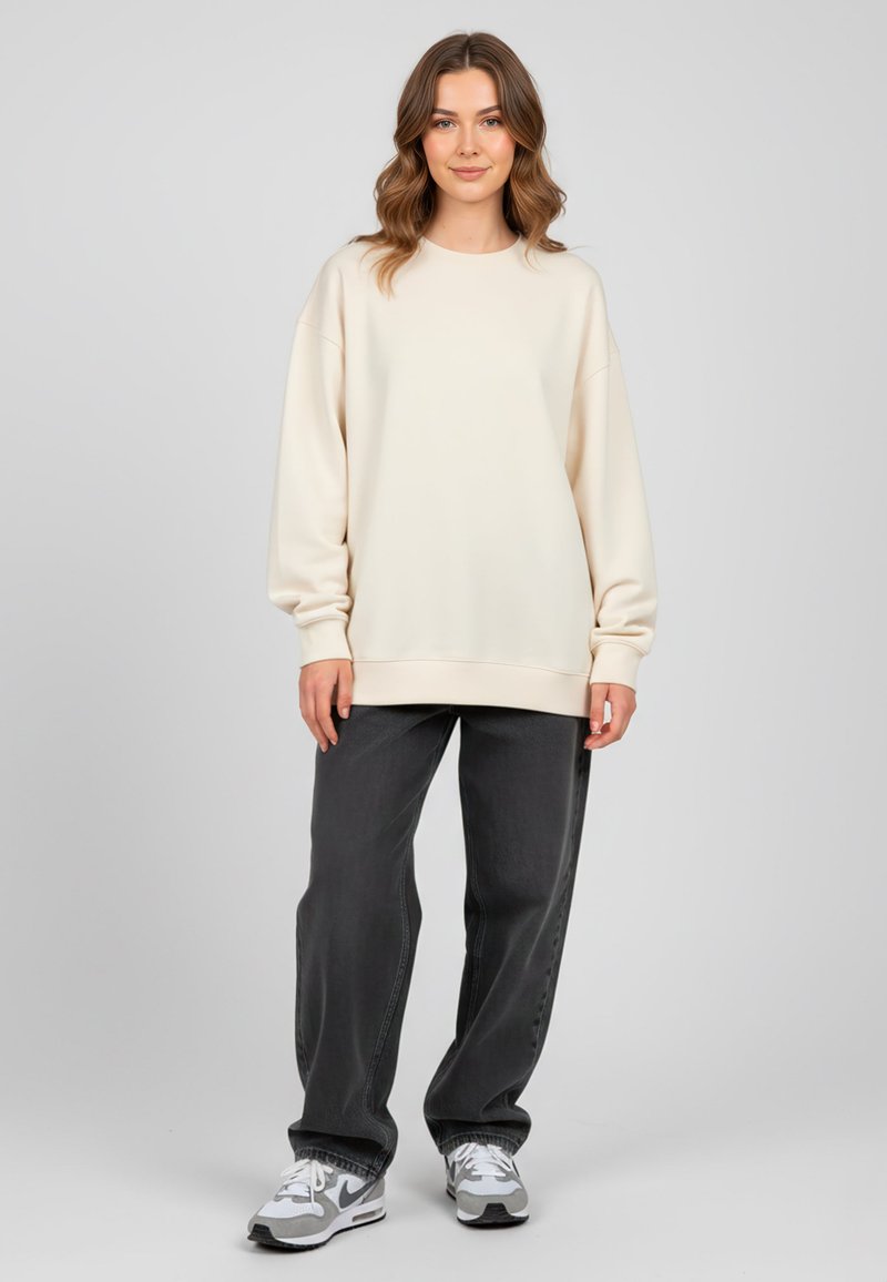 Felpa beige chiaro con vestibilità comoda e scollo rotondo. Abbinata a jeans larghi grigi scuri e sneakers grigie. Texture liscia.