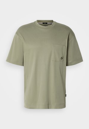 Camiseta de algodão verde oliva com decote redondo, mangas curtas e um bolso no peito com detalhe de logótipo bordado. Textura suave.