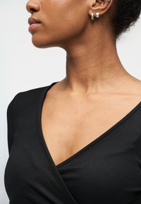 Μαύρο ριμπ μπλουζάκι με V-λαιμόκοψη. Λείο ύφασμα που αναδεικνύει το λαιμό. Ασημένια κρίκοι σκουλαρίκια συμπληρώνουν την εμφάνιση.