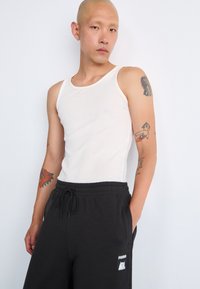 Hvid ribbet tanktop og sorte sweatpants med elastisk talje. Sweatpants har et lille Puma-logo på venstre ben.