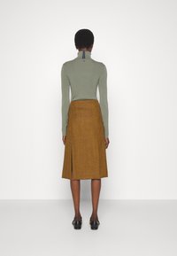 Grön långärmad topp med hög krage, kombinerad med en knälång senapsgul kjol med en sidoficka. Släta texturer och åtsittande design.