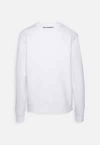 Felpa bianca con collo tondo, maniche lunghe, polsini e orlo a costine. Presenta un piccolo logo nero sulla parte superiore della schiena. Tessuto dalla texture liscia.