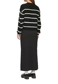Gestreifter Pullover in Schwarz und Weiß mit einem kurz geschnittenen Design, getragen über einem langen schwarzen Rock mit seitlichen Schlitzen, kombiniert mit klobigen schwarzen Schuhen.