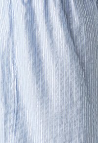 Světlomodrá látka s vertikálními bílými a kovově stříbrnými pruhy. Měkká textura s jemným leskem a jemnými záhyby.