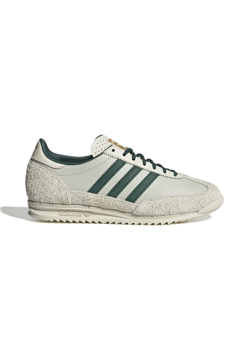 Baskets gris clair avec des accents en tissu blanc texturé, des rayures vert foncé, un bout arrondi et une semelle rembourrée affichant un logo au niveau du talon.